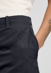Zwarte, lichte rok met een gladde textuur, met zichtbare riemlus en zijzakdetails. Close-up afbeelding van de taille naar beneden.