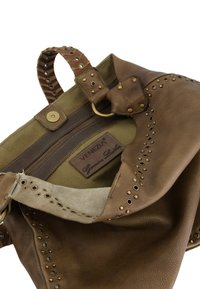 Sac en cuir marron avec quincaillerie en laiton, doublure en toile olive et accents de grommet décoratifs. Dispose d'un compartiment zippé et d'une poignée.