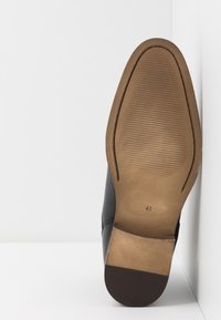 Černá kožená bota s hnědou gumovou podrážkou. Podrážka je hladká s drážkami a na spodní straně má označení velikosti "41".