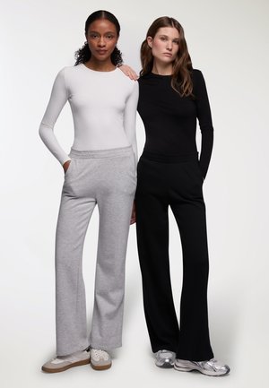 Due modelli stanno fianco a fianco, indossando maglie aderenti a maniche lunghe: una bianca e una nera. Abbinate a pantaloni tuta grigi e neri a vestibilità rilassata.