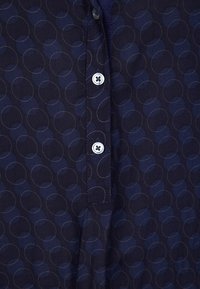 Short-sleeve shirt in dark navy fabric featuring a circular pattern, with a buttoned placket and light buttons. Soft texture, casual design.