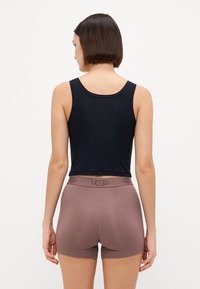 Black cropped tank top paired with light brown shorts featuring a UGG logo waistband, smooth texture, fitted shape, and minimalistic design.