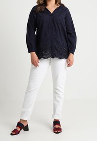 Blouse navy avec broderie florale et ourlet festonné, assortie à un jean droit blanc et des sandales à talons multicolores.