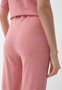 Rosa und beige gemustertes Stoffgewebe mit einem strukturierten, karierter Design; passgenaue Form mit einem sichtbaren Bund und einer Hand, die leicht an der Seite ruht.