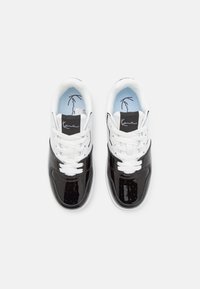 Svarta patentlädersneakers med vita snörningar och detaljer. Har en blå innerfoder och en signaturlogotyp på tungan.