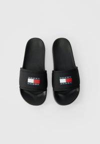 Black Tommy Jeans slide sandals with padded straps featuring the brand's red, white, and blue rectangular logo on each strap.