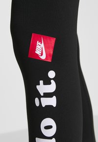 Svarta träningsleggings med en röd Nike-logotyp och vit text "Just Do It." Tyget är mjukt och har en åtsittande design.