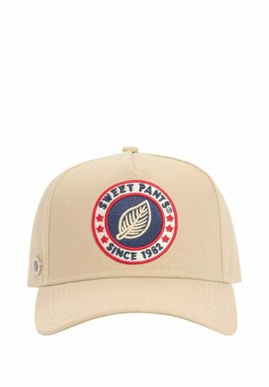 Casquette de baseball beige avec un patch circulaire montrant une feuille, des étoiles rouges et le texte "SWEET PANTS® DEPUIS 1982" sur le panneau avant.