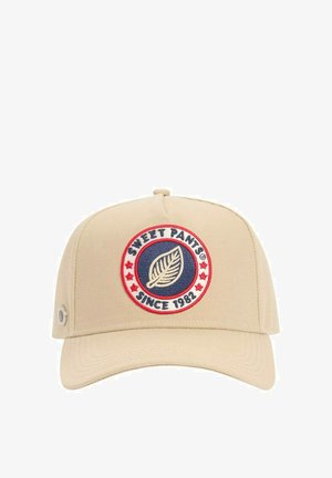 Casquette de baseball beige avec un patch circulaire montrant une feuille, des étoiles rouges et le texte "SWEET PANTS® DEPUIS 1982" sur le panneau avant.