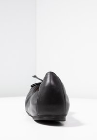 Mustat nahkakengät, joissa on kärjellinen muoto, matala heel ja koristeellinen nauha etuosassa, jotka ovat sileät ja minimalistiset.