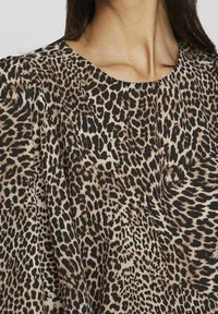Top a stampa leopardata con scollatura rotonda e vestibilità morbida, realizzato in tessuto morbido con tonalità di beige, nero e marrone in un motivo testurizzato.
