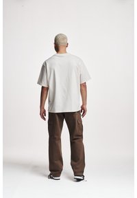 T-shirt en coton de couleur claire avec une coupe décontractée, associé à un pantalon cargo marron avec des poches latérales et une coupe droite.