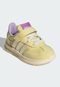 Yellow athletic shoe with white stripes, hook-and-loop strap, and purple accents. Made from suede and fabric with a rubber sole.