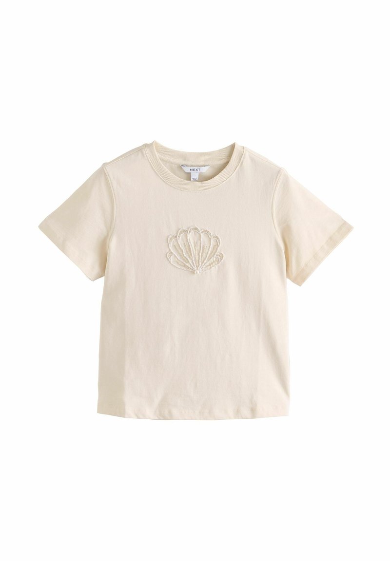 T-shirt court crème en coton avec col rond et motif coquillage brodé centré sur la poitrine.