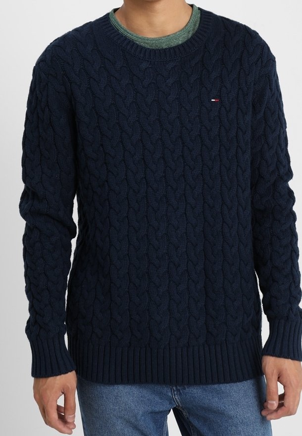 Navyblå kabelstickad tröja med ribbade cuffs och fåll, med en liten logotypdetalj. Ljusgrön rundhalsad skjorta lagd under.