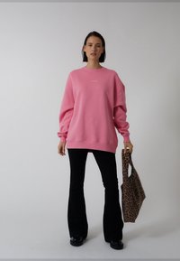Oversized rosa sweatshirt med långa ärmar och rund halsringning, kombinerad med svarta utsvängda byxor och en leopardmönstrad tygväska.