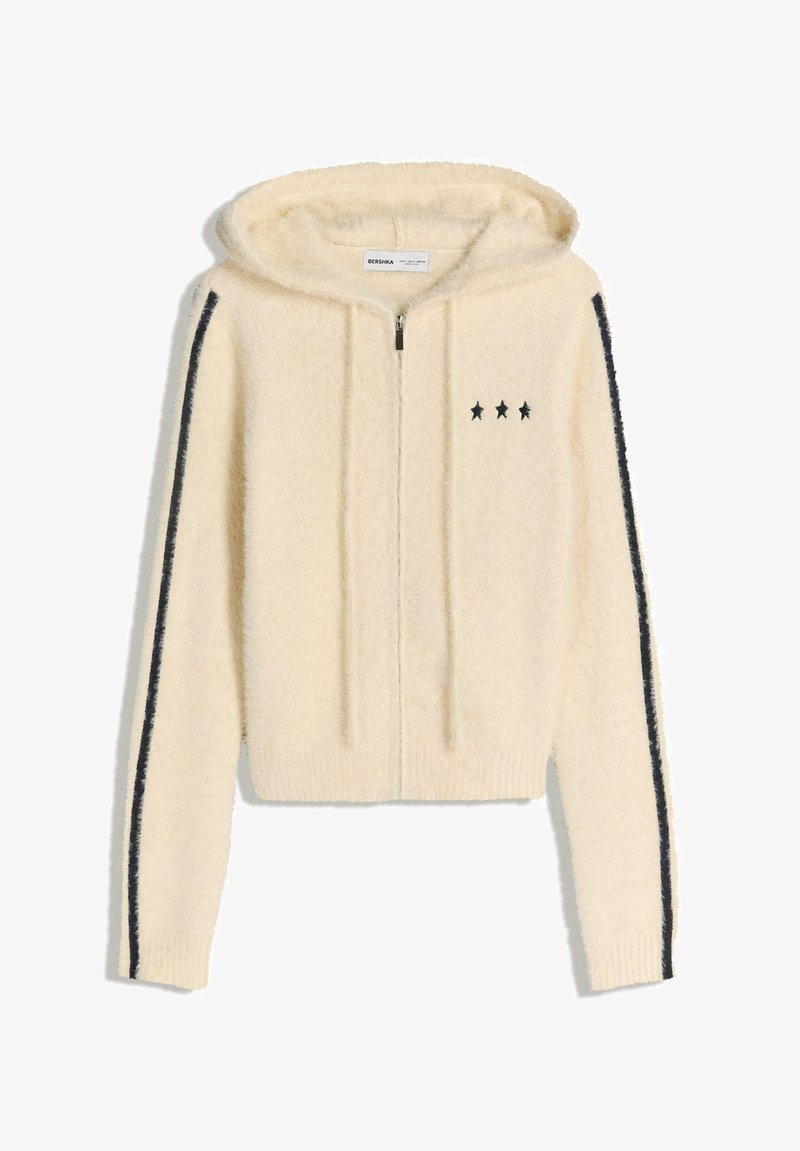 Hanorac din fleece crem, cu fermoar, având broderie cu stele negre pe piept și dungi negre pe mâneci.
