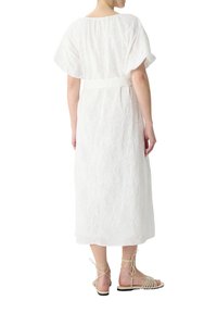 Weißes besticktes Kleid mit lockerer Passform, kurzen Ärmeln und Bindegürtel. Kombiniert mit beigen Riemchensandalen.