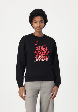 Schwarzer Sweatshirt mit roten Herzgrafiken und dem Schriftzug "Karl" in Weiß. Hergestellt aus einer Baumwollmischung, mit Rundhalsausschnitt und langen Ärmeln.