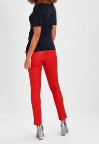 Black fitted t-shirt with short sleeves, paired with red slim-fit pants. Footwear features metallic silver heels. Smooth textures throughout.