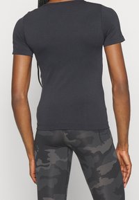 Maglietta nera a maniche corte con un design aderente, texture liscia e cuciture piatte, abbinata a leggings grigi con motivo camouflage.