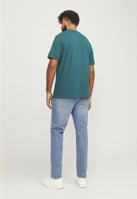 Teal short-sleeve t-shirt, relaxed fit, paired with light blue jeans and white sneakers. Simple design, cotton material, casual look.