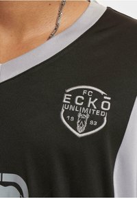 Maillot de sport noir avec des accents gris, arborant un logo ECKO UNLIMITED brodé et un design en V. Texture de tissu lisse.