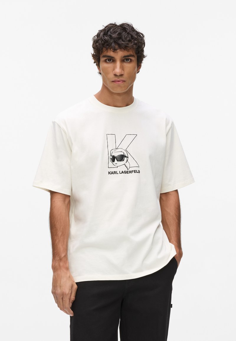 Biela bavlnená tričko s okrúhlym výstrihom, so čiernym grafickým znakom iniciál "K" a štýlovou tvárou so slnečnými okuliarmi. Krátke rukávy.
