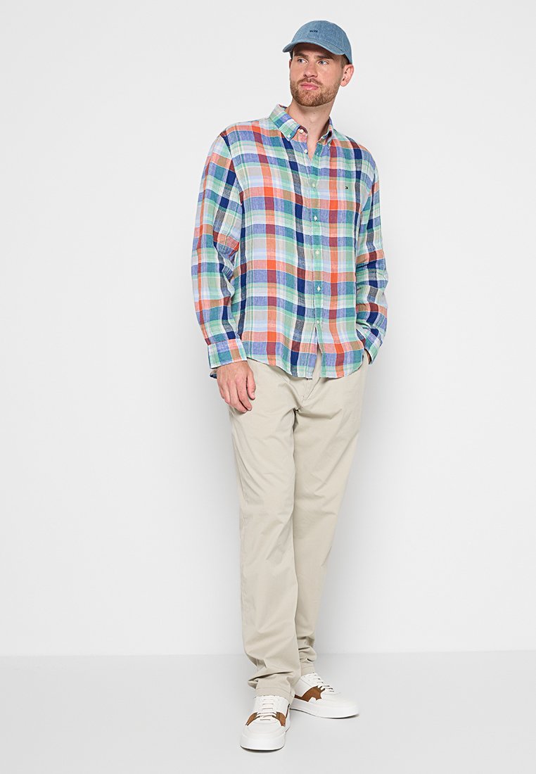 Herren kariertes Hemd in mehreren Farben mit hellblauem Grund, langen Ärmeln, Knopfleiste, kombiniert mit beigen Hosen und weißen Sneakers.