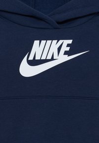 Tume sinine kapuuts, mis on valmistatud puuvillast ja millel on rindkeres suur valge Nike'i logo. Pehme tekstuur, koos kõhu tasku ja reguleeritava kapuutsiga.