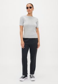 Top grigio a maniche corte abbinato a pantaloni neri e sneakers platform nere. Gli accessori includono occhiali da sole rotondi e orecchini ad anello. Tessuto dalla superficie liscia.