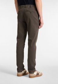 Donkerbruine, slim-fit broek met twee achterzakken en knoopsluitingen. Draag met beige sneakers met bruine accenten.