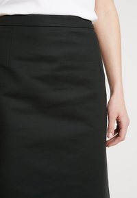 Svart blyertskjol med en slät textur, som har en figurnära design och ett midjeband, når knä längd, i kombination med en vit topp.