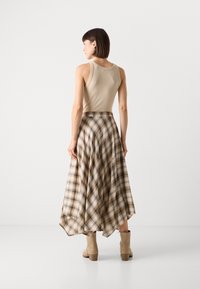 Beige tætsiddende tanktop kombineret med en plaid, svævende midi-nederdel i beige og afdæmpede nuancer, suppleret med beige ankelstøvler.