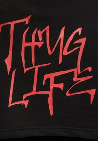 Black fabric with bold, stylized red lettering saying "Thug Life." The design features sharp angles and a textured finish.