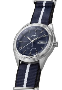 Het Timex Marlin-horloge heeft een zilverkleurige roestvrijstalen kast, een marineblauwe wijzerplaat, witte accenten en een marineblauwe gestreepte stoffen band met weergave van dag en datum.