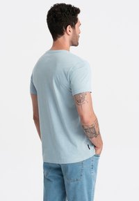 Světle modré bavlněné tričko s kulatým výstřihem a krátkými rukávy, které má jemnou strukturu. Pohled zezadu odhaluje štíhlý střih a minimální branding.