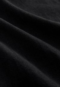 Tissu en coton noir avec une texture douce, présentant des plis délicats et une surface lisse, mettant en valeur sa couleur riche et profonde.