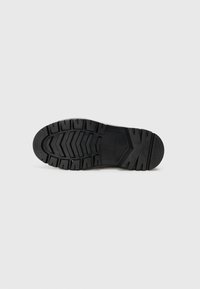 Semelle de chaussure en caoutchouc noir avec des motifs de crampons profonds. Contient plusieurs rainures pour une meilleure adhérence. Design plat avec une texture subtile sur les bords.