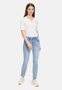 Haut blanc à manches courtes avec un col henley et un détail de boutons, associé à un jean slim bleu clair et des baskets blanches.