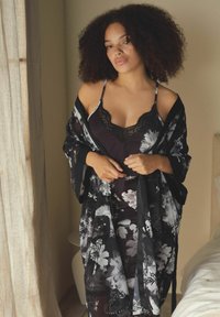 Kimono negru cu flori, realizat dintr-un material ușor, peste o rochie slip întunecată, cu detalii din dantelă. Ambele articole au un design fluid.