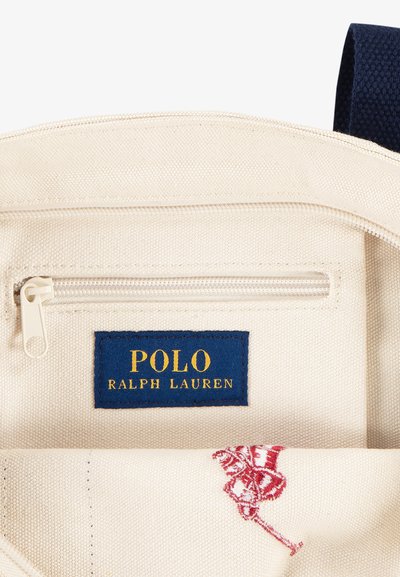 Bežani platneni interijer sadrži zip džep i plavu oznaku s natpisom "POLO RALPH LAUREN" u zlatnoj boji. Vidljiv je crveni izvezeni dizajn.