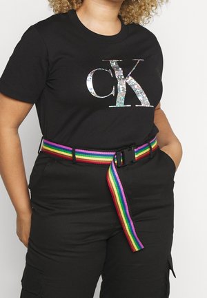 Person wearing black Calvin Klein t-shirt with holographic logo, black pants, and a rainbow-striped fabric belt with a black buckle.