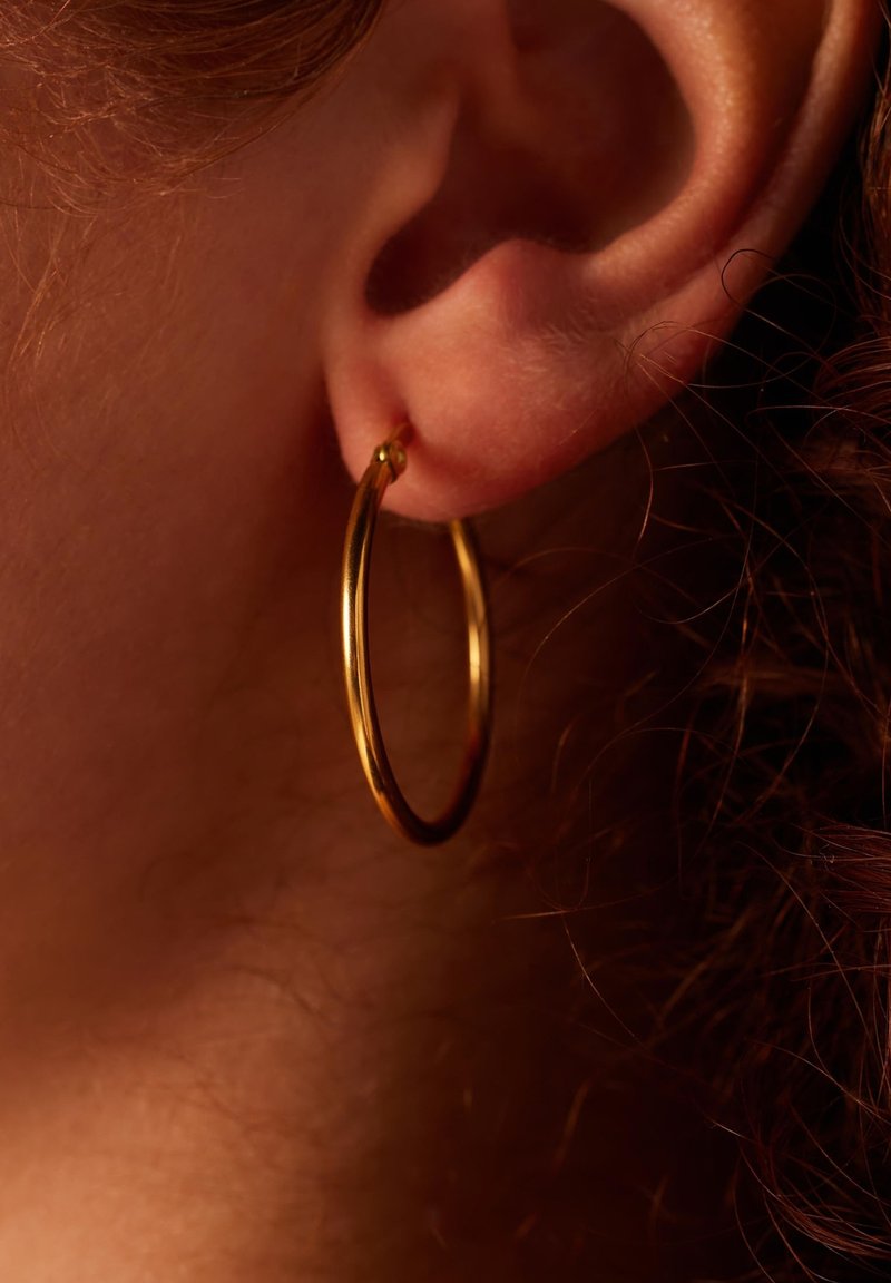 Gouden creolen bevestigd aan de oorlel, met een gladde, glanzende oppervlakte en ronde vorm met een onopvallend sluitdetail.