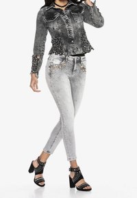 Harmaa farkkutakki korostetuin hihoin, yhdistetty kuluneisiin harmaisiin farkkuihin, joissa metallisia yksityiskohtia. Mustat korolliset sandaalit niiteillä.