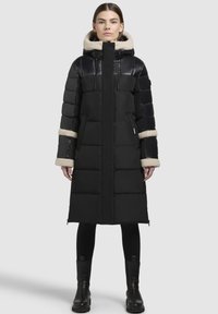 Schwarze Pufferjacke mit langer Silhouette, glänzendem Oberteil und plüschiger beiger Kapuze. Verfügt über gerippte Bündchen, Seitentaschen und Reißverschlüsse.