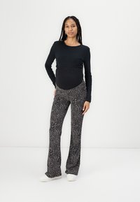Svart langermet topp i elastisk stoff, kombinert med mønstrede bukser med utsving i svart og hvitt zebra-striper, brukt med hvite joggesko.