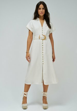 Robe en lin blanc avec col, manches courtes, boutons sur le devant et une ceinture large avec une boucle circulaire ; escarpins compensés avec bride de cheville.