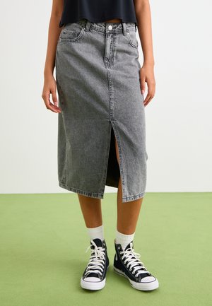 Grå denimskjørt med frontspalte og høy midje, stylet med svarte høye sneakers og hvite sokker på et grønt gulv.