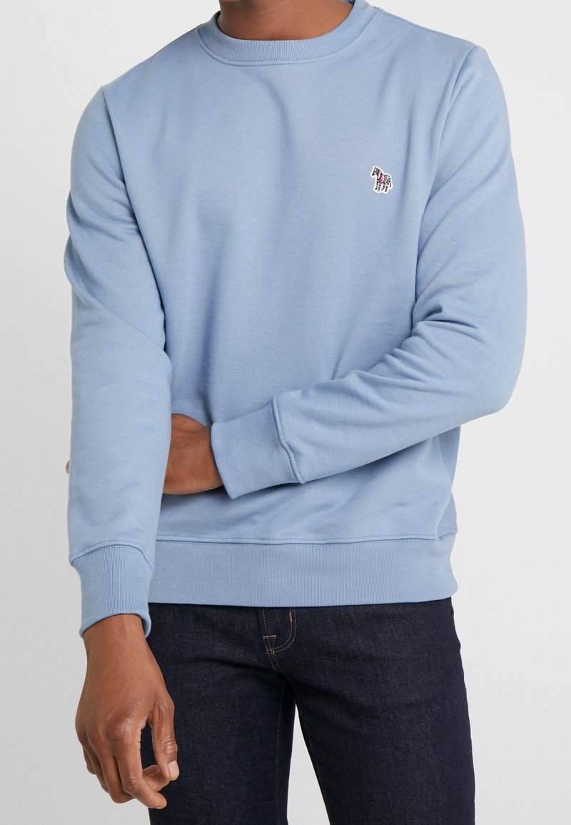 Felpa blu chiaro con collo rotondo, polsini e orlo a costine. Presenta un piccolo logo a motivo sul lato sinistro del petto. Materiale in morbido misto cotone.